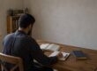 Читатель изучает открытый Коран и делает заметки за деревянным столом в домашнем уголке для чтения